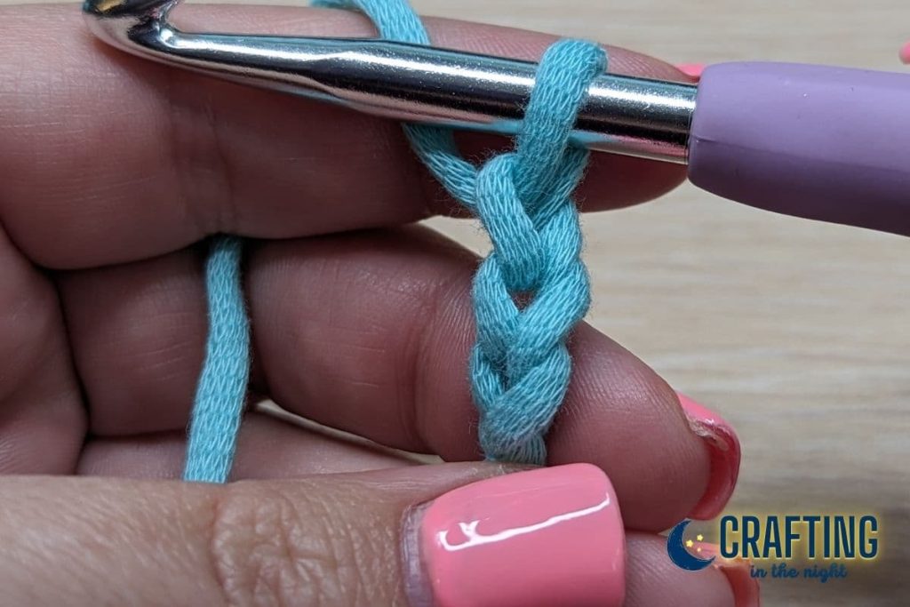 Step 1. A hand holding a blue yarn with a crochet hook making a slip knot and chain 3.