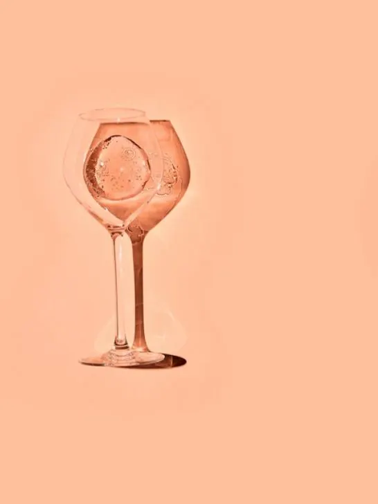 clear wine glass with champagne on a peach fuzz background