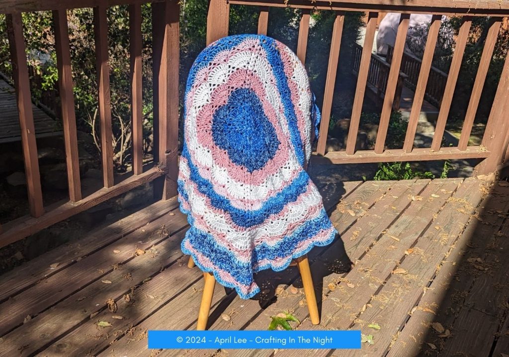 Blue with pink Flora Blossom Crochet Blanket draped over a chair.