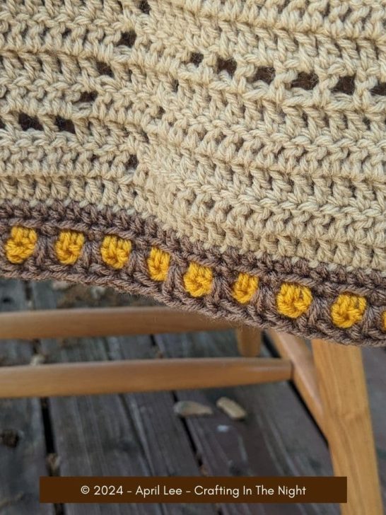 bottom edge of a filet crochet blanket that has the moroccan tile stitch border in the colors gold and brown